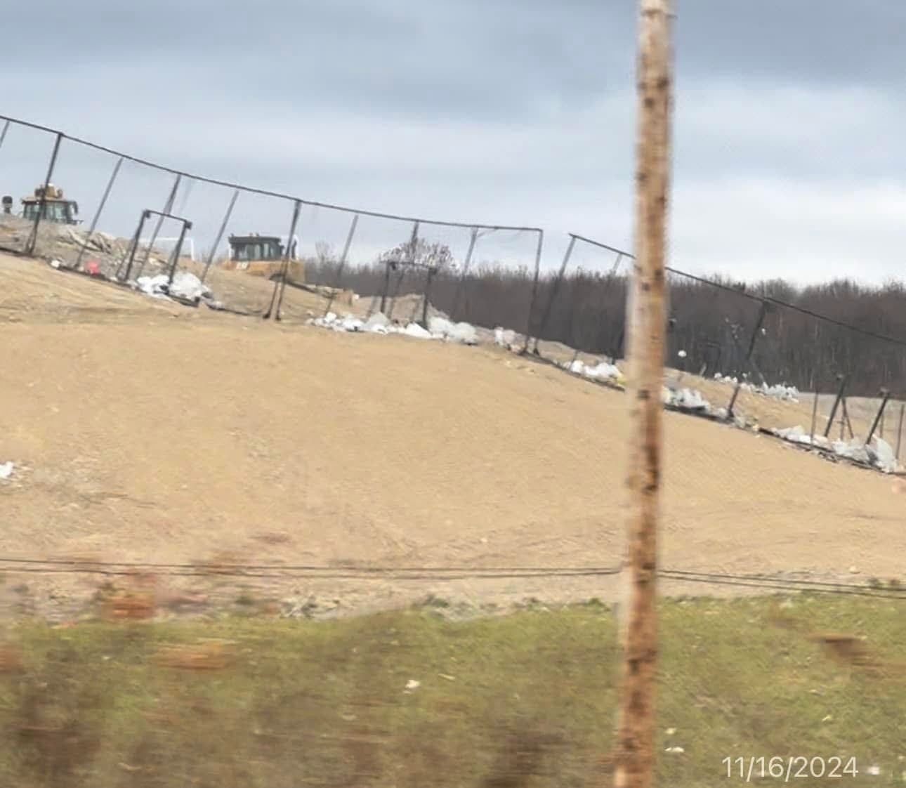 A bulldozer working on an active landfill cell, debris piled along the perimeter fence.