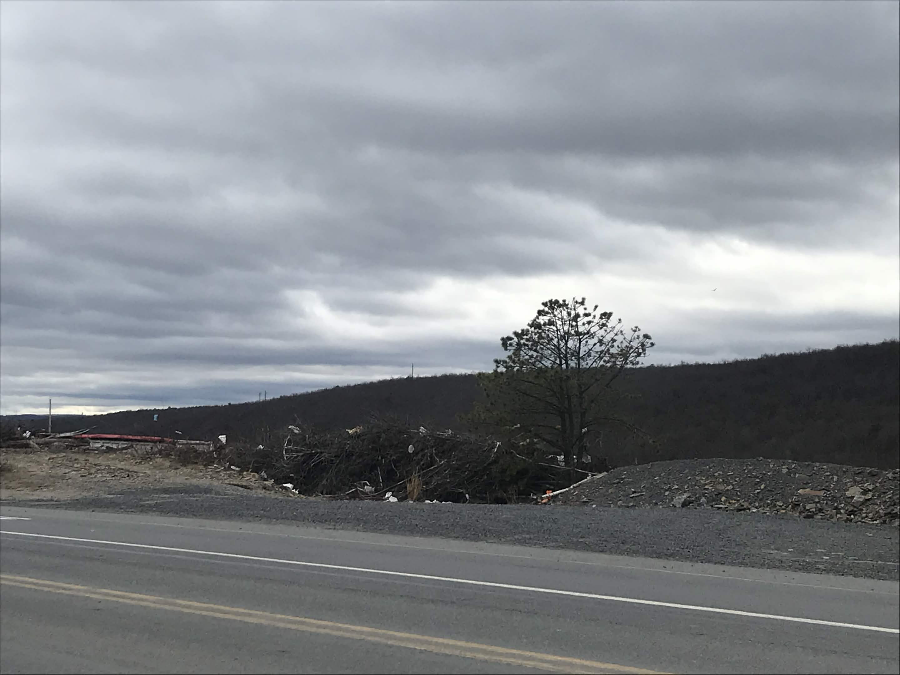 A debris ridge along a public road in Schuylkill County: scattered waste against a dead tree and an overcast sky.
